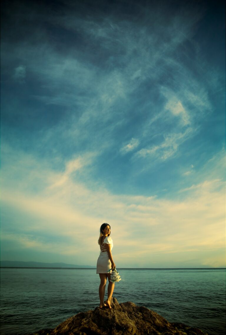 a woman standing on top of a rock near the ocean